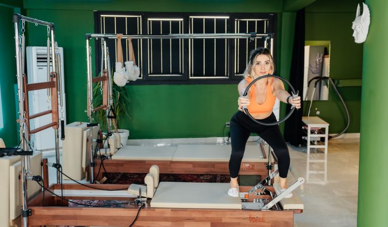Fitness enthusiast practicing Pilates on a reformer machine in a modern, brightly lit studio.